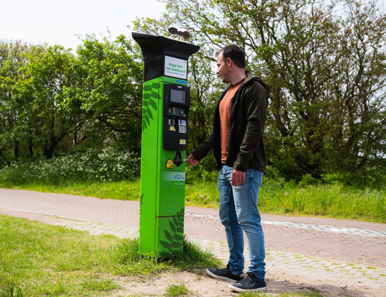 Een man koopt een duinkaart bij een duinkaartautomaat in het duin.